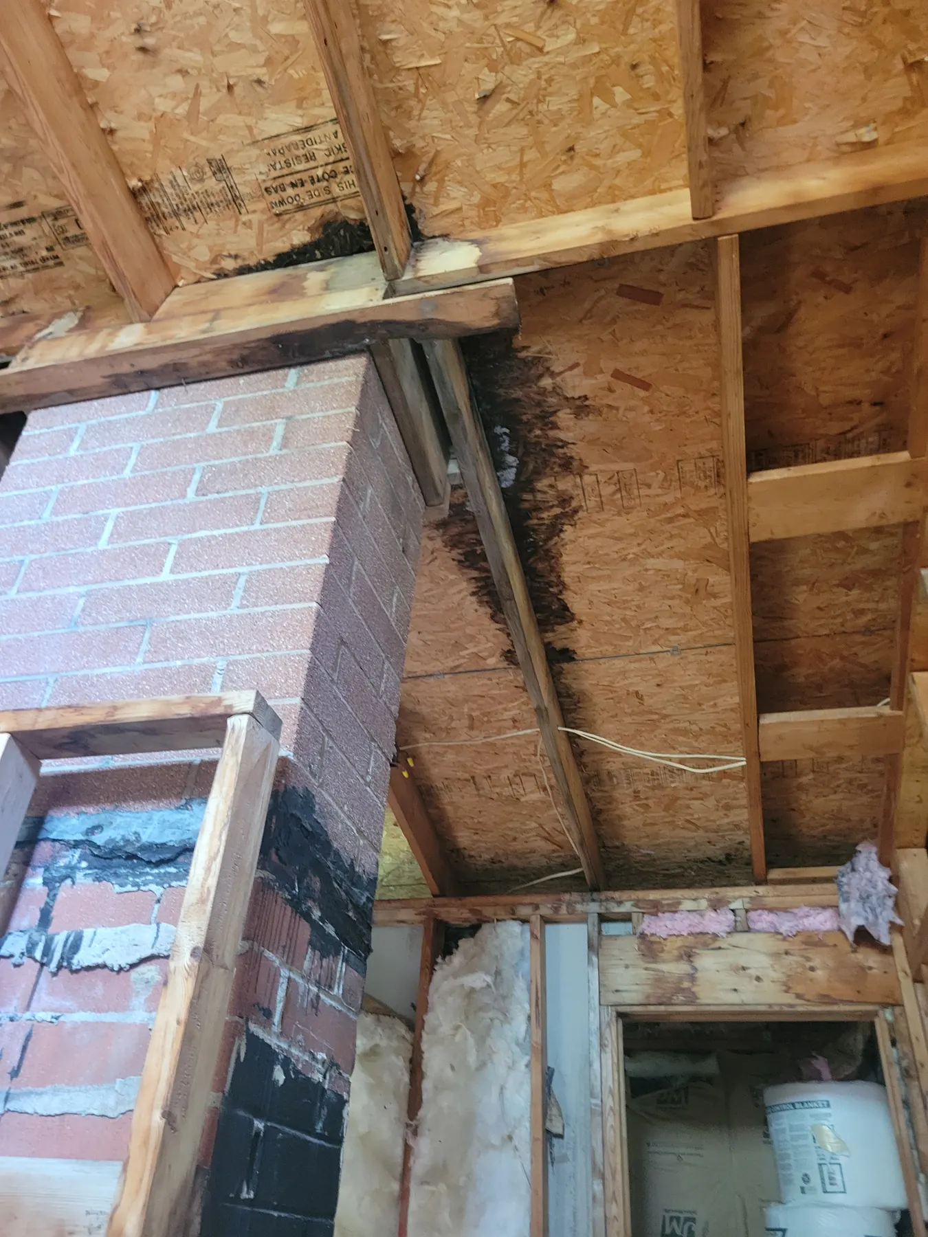 Exposed roof framing and visible water-related deterioration near the chimney at 2077 Elliott Street